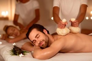 Spouses Enjoying Herbal Back Massage And Aromatherapy Lying And Relaxing In Spa Center Indoors. Masseur Massaging Couple Using Bags With Aromatic Herbs. Exotic Relaxation. Selective Focus - Best cities for New Year's Eve celebration with family 2021 last minute gifts unique gifts card for couples, Spa massage in New York City, Manhattan
